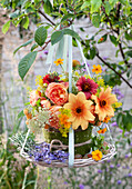 Summer bouquet in flame color: roses, simple dahlias, Blanket flowers, yellow bedstraw, golden marigolds, Queen Anne's Lace, and yellow raspberries in basket with felt covering on bowl, hung on branch with ribbon, lavender flowers and gooseberries as decoration