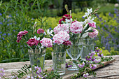 Small bouquets of carnation blossoms and candles as table decoration placed on a board and decorated with tendrils of crown vetch