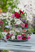 Self-made etagere made of zinc coasters and glasses as fragrant table decoration with carnation blossoms and oregano blossoms