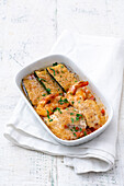 Gratinated courgettes, prawns and fish fillets in a casserole dish