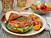 Chicken burger on a pretzel bun with lettuce, red onions and herbed cherry tomatoes