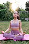 Young woman meditating on yoga rug in garden