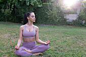 Young woman relaxing in yoga lotus pose at garden