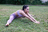 Young woman in sportswear stretching in garden on grass