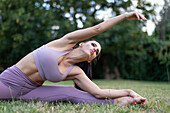 Woman in sportswear stretching in garden on grass