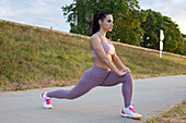 Young woman doing lunge warm up exercise at embankment