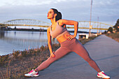 Young jogger woman stretching legs before run at riverside