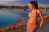 Young sporty woman with hula hoop at riverbank