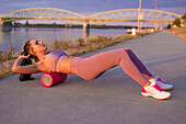 Young woman doing exercise by foam roller at riverbank
