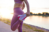 Runner woman stretching leg in sunrise at riverside