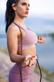 Young athlete woman holding jump rope at riverbank