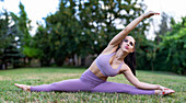 Woman doing yoga splits stretching on meadow