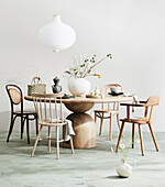 Various chairs around round wooden table with vase and asitatic place setting