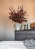 Vintage vase of autumn branches on dresser against pale painted wall