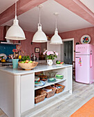 Large industrial style pendant lights and a pink fridge in a bright kitchen with walls in shades of pink