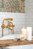 Board as bath caddy with white candles in the bathroom with a golden faucet