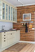 Cream-coloured kitchen cupboards with glass-fronted wall units and rough wooden wall in the kitchen