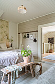 Doppelbett mit silberfarbener Tagesdecke und alte Holzbank mit Geranie im Schlafzimmer