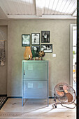 Metal cupboard, with a photo gallery below and fan in the living room