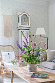 Gemütliches Wohnzimmer mit Standuhr und heller Tapete, Sommerblumenstrauß auf Couchtisch