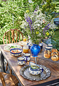 Wooden table with blue and white ceramic dishes, freshly baked rolls, and bouquet of meadow flowers