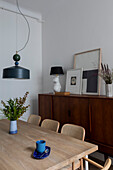 Dining table with oak top below pendant light and in front of mid-century sideboard in dining room