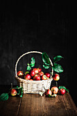 Korb mit Äpfeln auf Holztisch vor schwarzem Hintergrund
