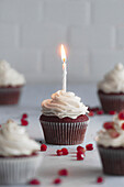 Red-Velvet-Cupcakes mit Granatapfelkernen und brennender Kerze