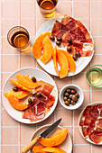Prosciutto, cantaloupe and white wine over pink table