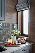 Flowers, breadboard and fresh eggs on kitchen base units below grey splashback with subway tiles and wood panelling