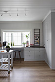 Light grey fitted furniture and table on castors in pale kitchen with wood panelling