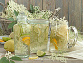 Mehrere Gläser Holunderblütensirup mit Limetten, Zitronen und Orangenscheiben