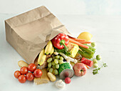 A brown paper shopping bag fallen over with different types of food from the grocery store