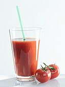 A glass of tomato juice with a straw, tomatoes next to it