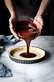 A baker pouring melted chocolate ganache into a tart shell