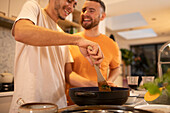 Happy gay male couple cooking in kitchen