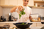 Young man cooking with fresh spinach in kitchen