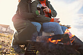 Couple in winter coats drinking red wine by beach fire
