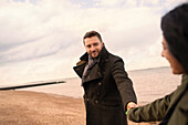 Couple in winter coats holding hands on beach