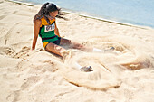 Female track and field athlete long jumping into sand