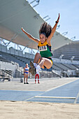 Female track and field athlete long jumping over sand