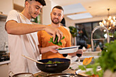 Gay male couple cooking with fresh spinach in kitchen