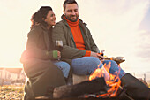 Happy couple enjoying red wine by fire on winter beach