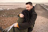 Happy couple in winter coats hugging on ocean jetty