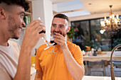 Happy gay male couple drinking red wine in kitchen