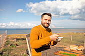 Happy man eating on sunny ocean beach patio