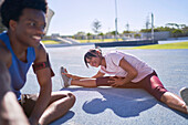 Happy young runners stretching on sunny sports track