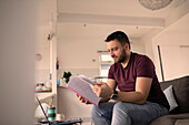 Man with paperwork working from home on laptop on sofa
