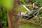 Man working on laptop in lawn chair in summer garden