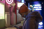 Woman using smart phone on city sidewalk at night